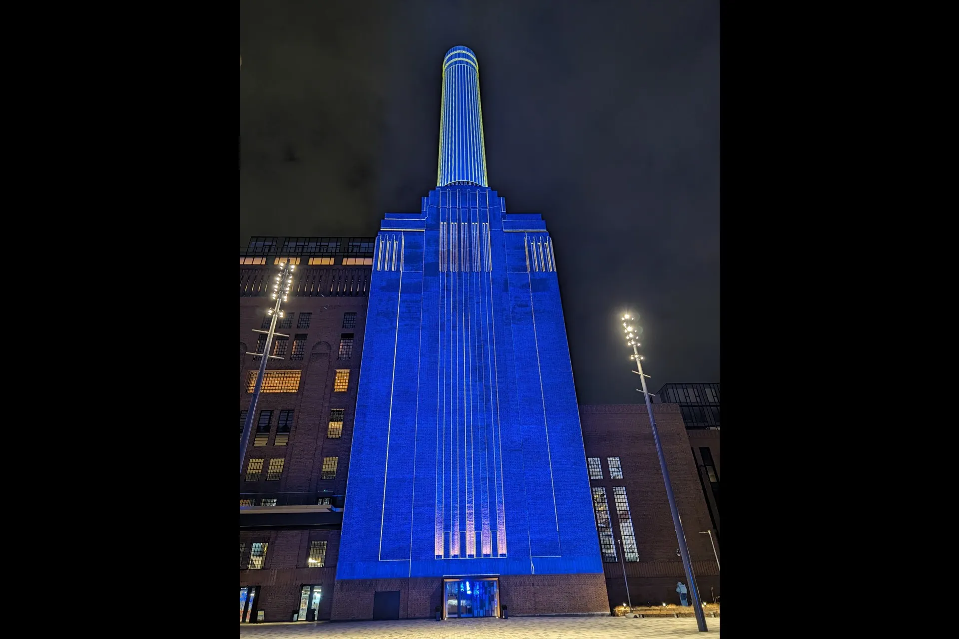 one tower of Battersea Power Station at night, its facade and chimney lit in blue with fine gold lines